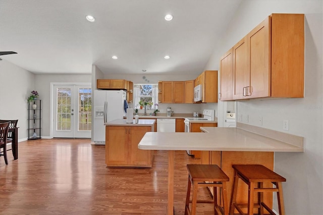 kitchen featuring sink, a kitchen island, a breakfast bar, light wood-type flooring, and white appliances