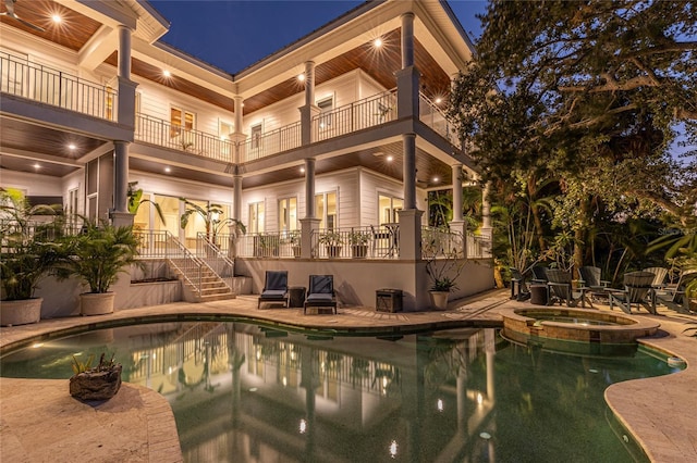 pool at night with an in ground hot tub and a patio area