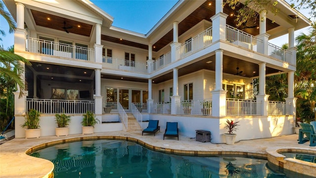 back of property featuring ceiling fan, a patio area, a swimming pool with hot tub, and a balcony