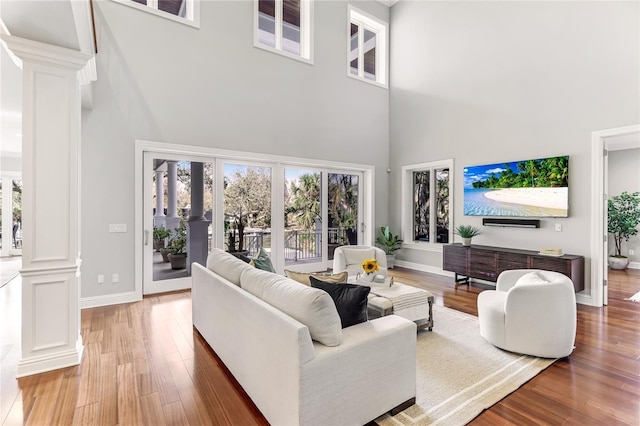 living room with hardwood / wood-style flooring, french doors, ornate columns, and a towering ceiling