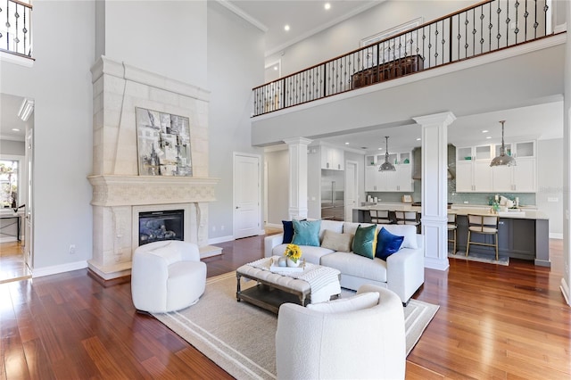 living room with crown molding, wood-type flooring, a premium fireplace, and a high ceiling