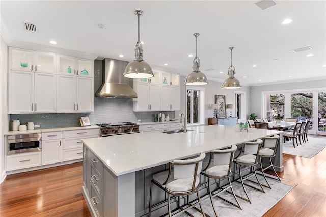 kitchen with white cabinets, wall chimney exhaust hood, double oven range, sink, and a large island