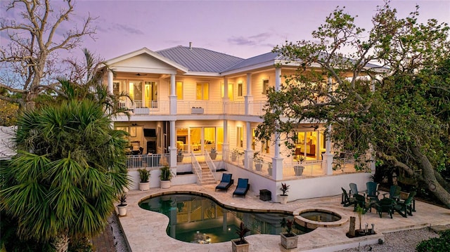 back house at dusk with a balcony, a patio area, a swimming pool with hot tub, and ceiling fan