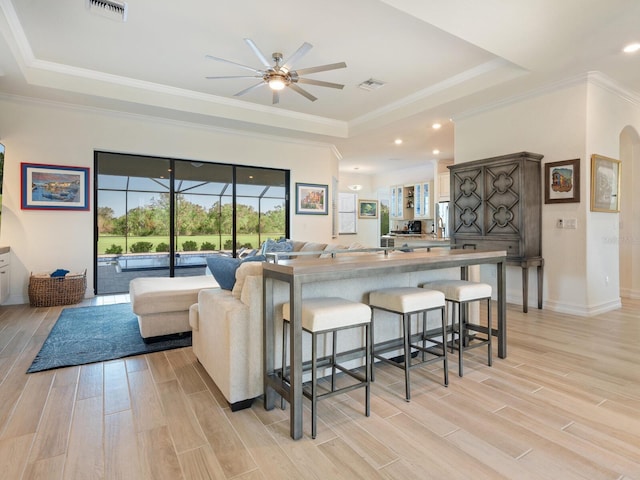 kitchen featuring a raised ceiling, stainless steel refrigerator with ice dispenser, a breakfast bar, and light wood-type flooring