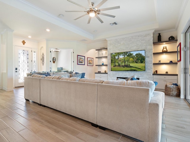 living room with a raised ceiling, crown molding, built in features, and ceiling fan