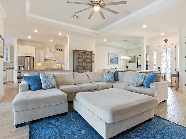 living room featuring ceiling fan, ornamental molding, a raised ceiling, and light wood-type flooring