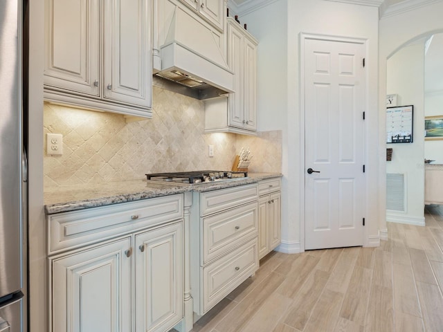 kitchen featuring light stone counters, crown molding, custom exhaust hood, and light wood-type flooring