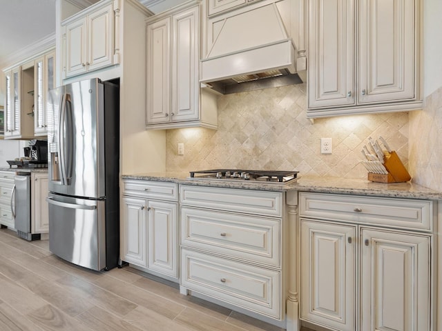 kitchen featuring tasteful backsplash, appliances with stainless steel finishes, custom range hood, and light stone counters