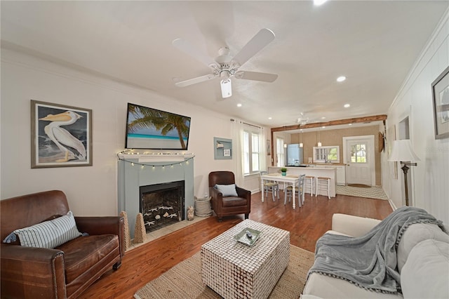 living room with wood-type flooring, ornamental molding, and ceiling fan