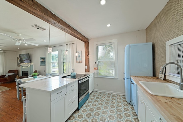 kitchen featuring pendant lighting, beamed ceiling, white cabinetry, sink, and stainless steel range with electric cooktop