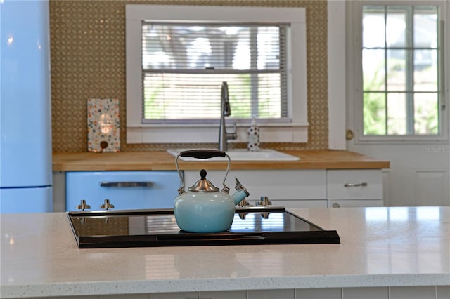 kitchen featuring white refrigerator, light stone countertops, sink, and white cabinets