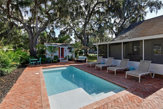 view of pool featuring an outbuilding, a patio area, and a sunroom