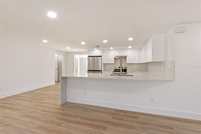 kitchen with stainless steel appliances, kitchen peninsula, backsplash, white cabinetry, and light hardwood / wood-style flooring