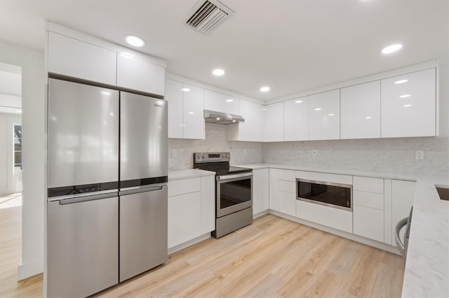 kitchen featuring stainless steel appliances, white cabinetry, light hardwood / wood-style flooring, and decorative backsplash