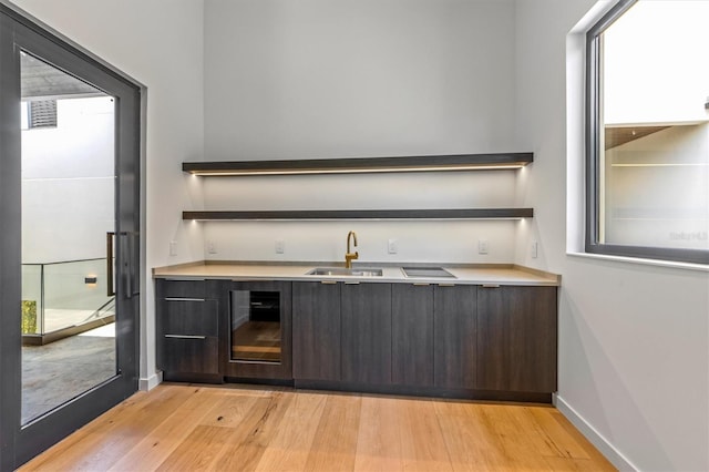 bar with dark brown cabinets, wine cooler, sink, and light wood-type flooring