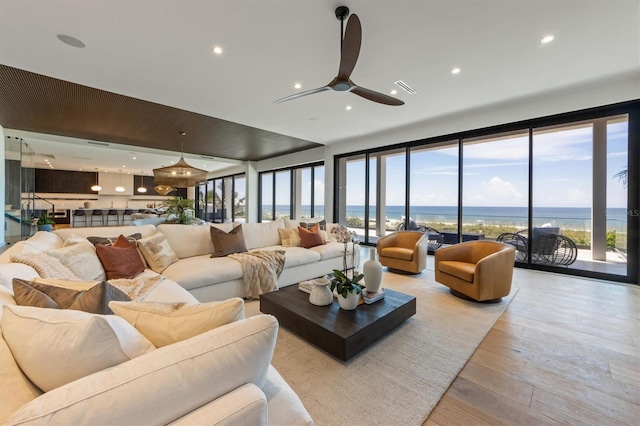 living room with ceiling fan, a healthy amount of sunlight, a water view, and light hardwood / wood-style flooring