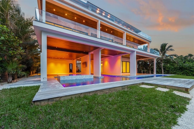 back house at dusk featuring a balcony, a patio, and a yard