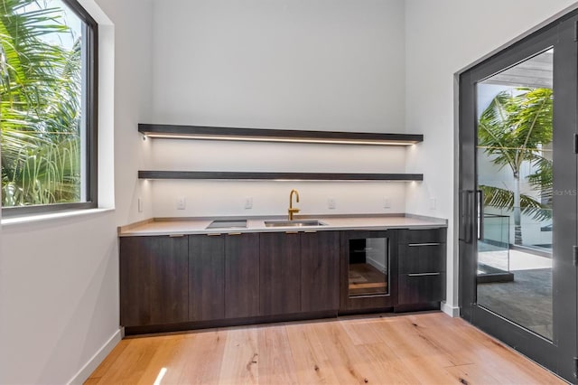 bar with dark brown cabinets, light hardwood / wood-style floors, sink, and beverage cooler