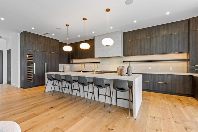 kitchen with an island with sink, light hardwood / wood-style floors, a kitchen breakfast bar, and pendant lighting