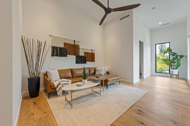 living room with light wood-type flooring, ceiling fan, and a high ceiling