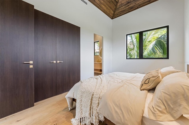 bedroom with light wood-type flooring, ensuite bath, and high vaulted ceiling