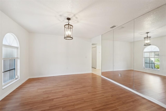 unfurnished room featuring hardwood / wood-style flooring, a textured ceiling, and an inviting chandelier