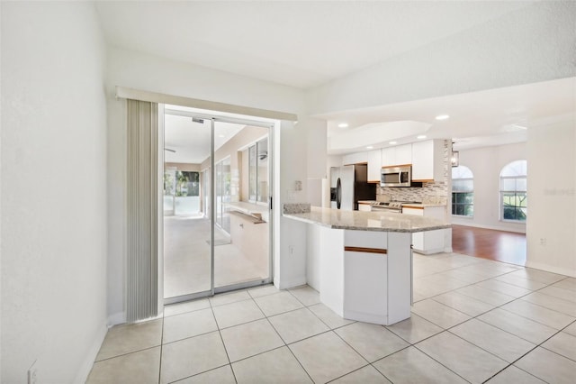 kitchen featuring light stone counters, light tile patterned flooring, white cabinetry, appliances with stainless steel finishes, and kitchen peninsula