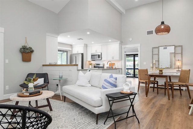 living room featuring recessed lighting, a high ceiling, visible vents, baseboards, and light wood-style floors