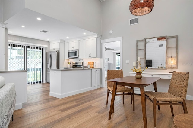 dining room featuring ceiling fan, light hardwood / wood-style floors, and a towering ceiling