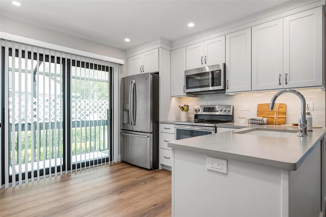 kitchen featuring stainless steel appliances, backsplash, a sink, light wood-type flooring, and a peninsula