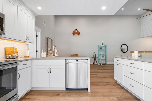 kitchen with light wood finished floors, visible vents, a peninsula, stainless steel appliances, and a sink