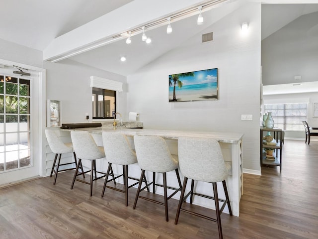 kitchen featuring a kitchen bar, kitchen peninsula, dark hardwood / wood-style flooring, and vaulted ceiling