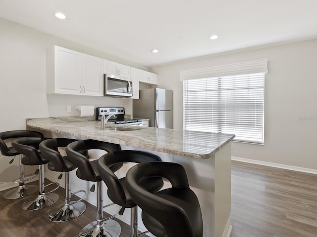 kitchen featuring stainless steel appliances, white cabinetry, kitchen peninsula, a breakfast bar area, and dark hardwood / wood-style flooring