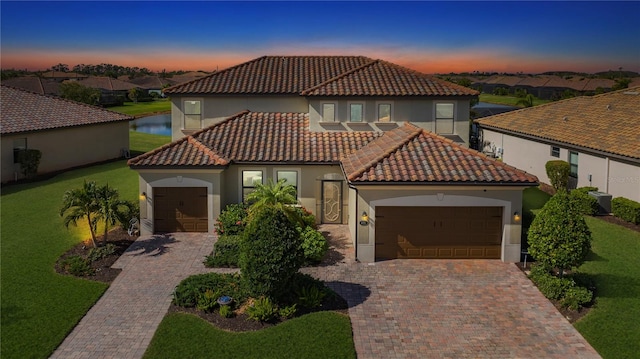 mediterranean / spanish-style home featuring decorative driveway, a tile roof, a yard, stucco siding, and an attached garage