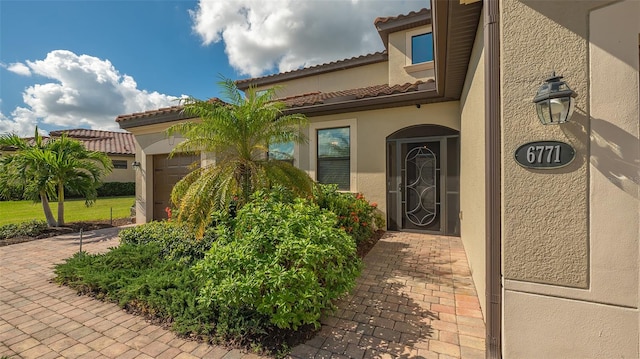 doorway to property with a garage, decorative driveway, a tiled roof, and stucco siding