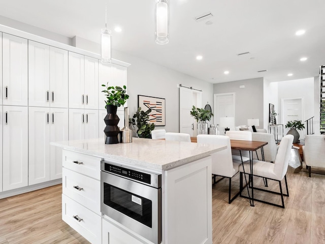 kitchen featuring white cabinets, light stone countertops, light wood-type flooring, pendant lighting, and a center island