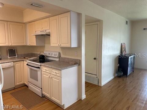 kitchen featuring white appliances, under cabinet range hood, light wood-style flooring, and baseboards
