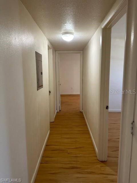 corridor with electric panel, a textured ceiling, light wood finished floors, and baseboards
