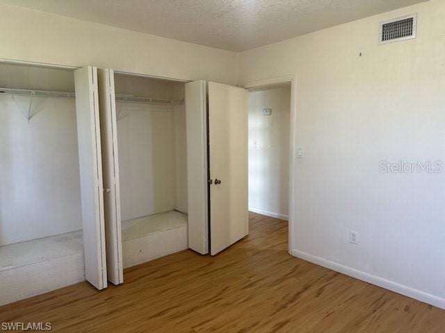 unfurnished bedroom featuring two closets, wood finished floors, and baseboards
