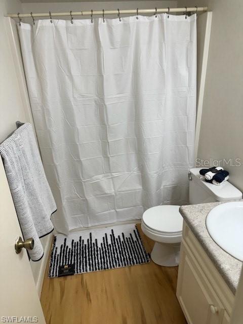 bathroom with wood finished floors, toilet, vanity, and a shower with shower curtain