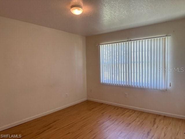 empty room featuring wood finished floors, baseboards, and a textured ceiling