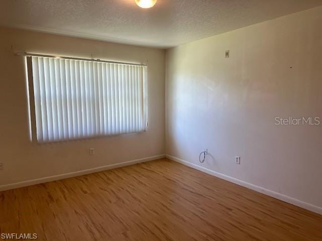 empty room featuring wood finished floors, baseboards, and a textured ceiling