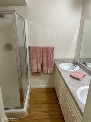 full bathroom with wood finished floors, a stall shower, double vanity, and baseboards
