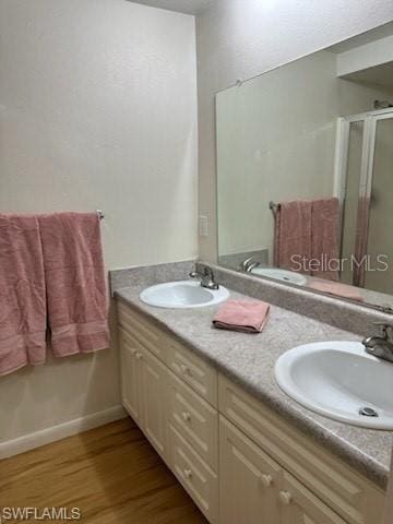 full bathroom with wood finished floors, a shower stall, and double vanity