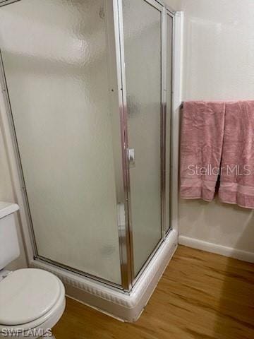 bathroom with wood finished floors, a stall shower, toilet, and baseboards