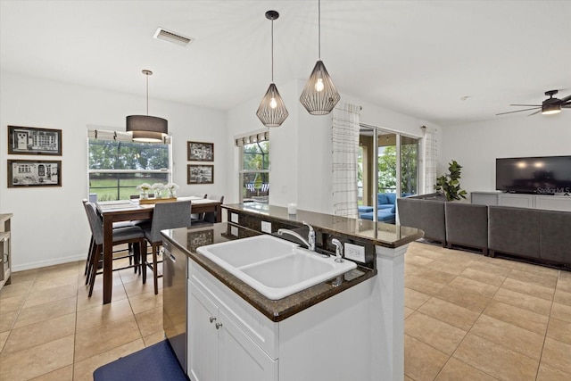 kitchen featuring dark countertops, hanging light fixtures, white cabinets, a sink, and an island with sink