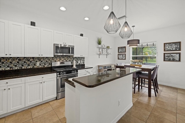 kitchen featuring white cabinetry, appliances with stainless steel finishes, a center island, dark countertops, and decorative light fixtures