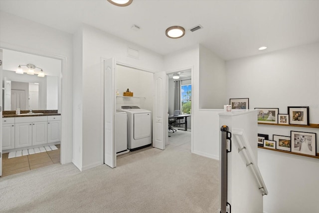 hall with light colored carpet, a sink, visible vents, an upstairs landing, and washer and clothes dryer