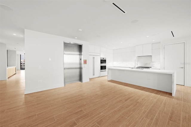 unfurnished living room with elevator, sink, and light wood-type flooring