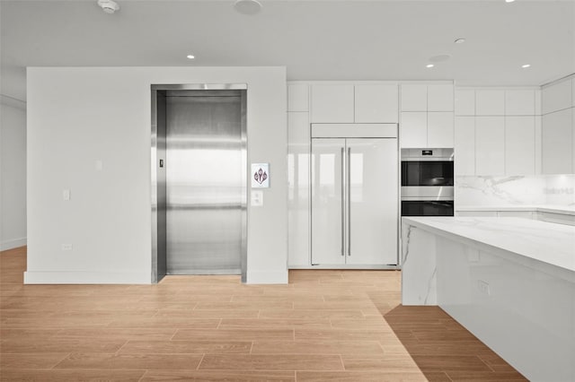 kitchen with white cabinetry, paneled built in fridge, elevator, and light wood-type flooring